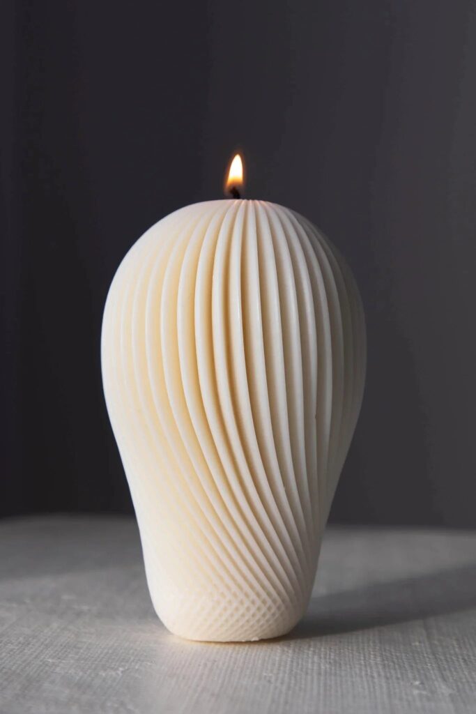 Ivory ribbed swirl candle with a lit wick
