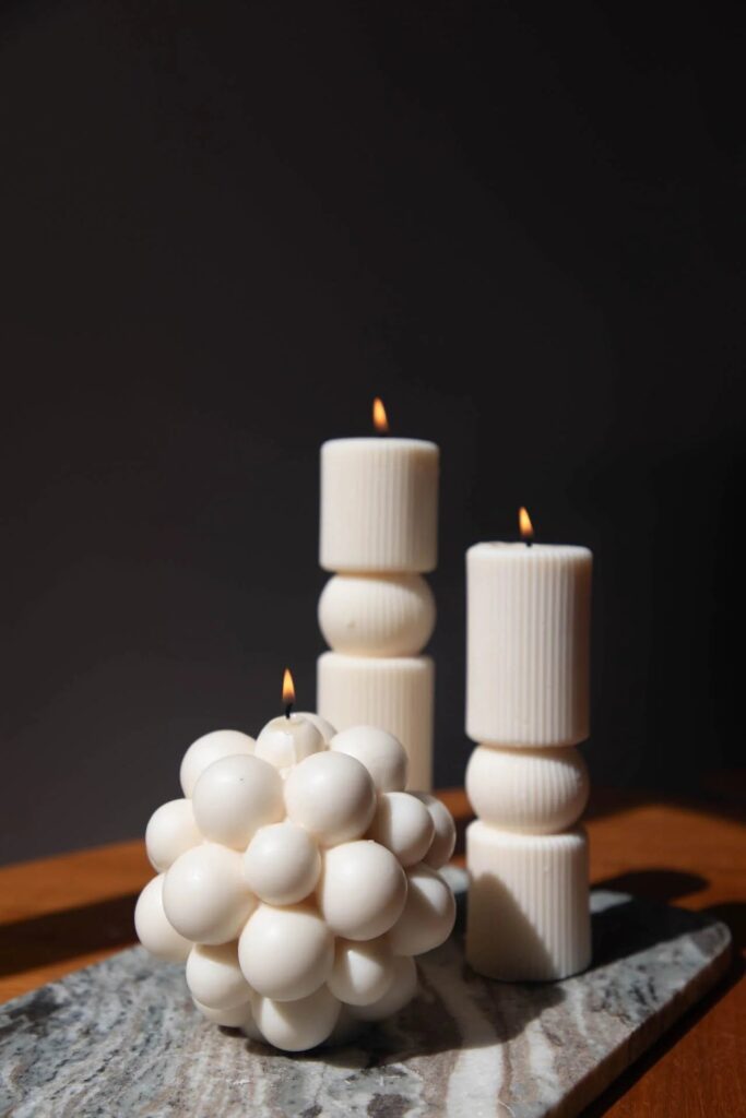 Ivory bubble cube candle beside ribbed pillar candles on marble