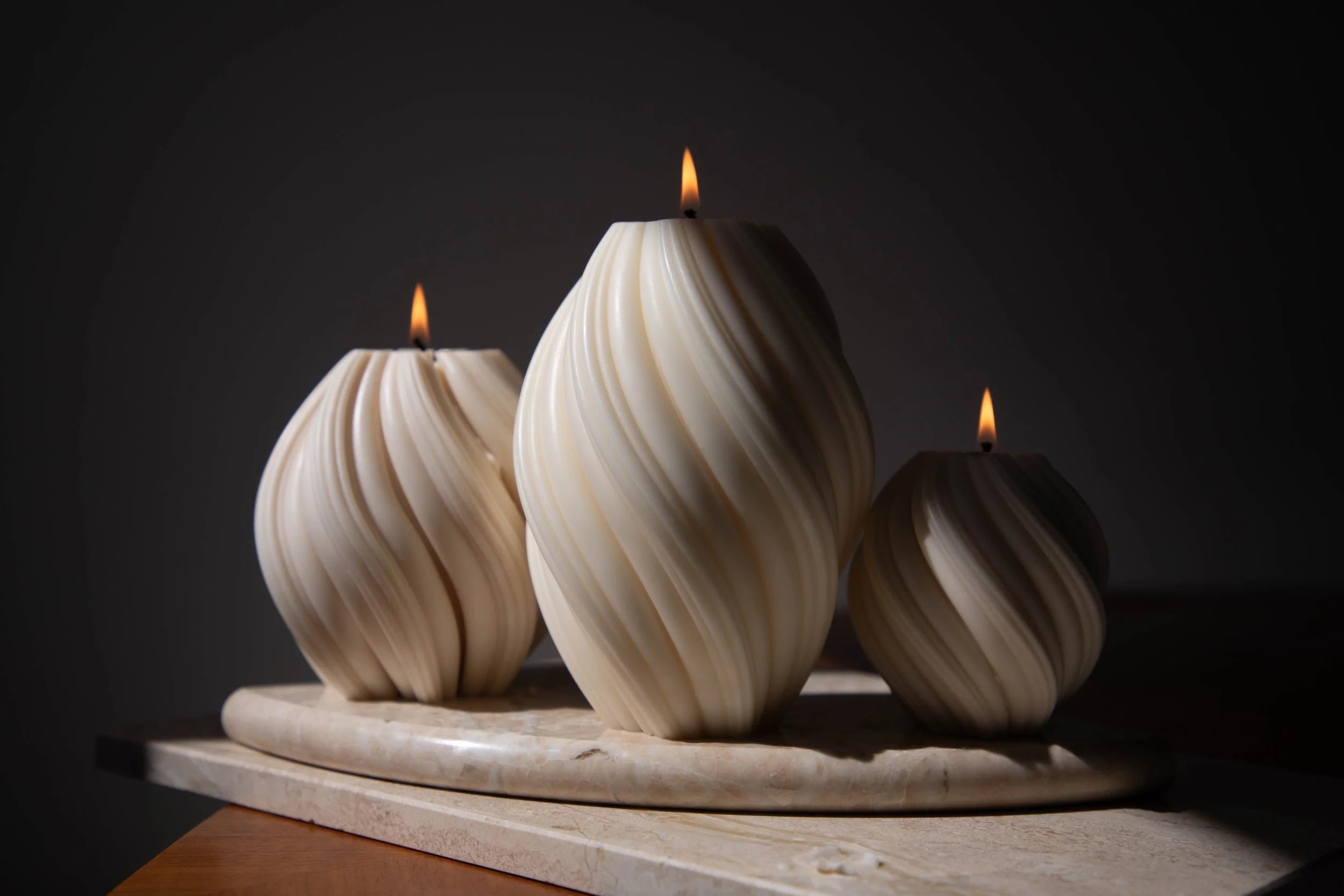 Three ivory swirl candles lit on a stone tray